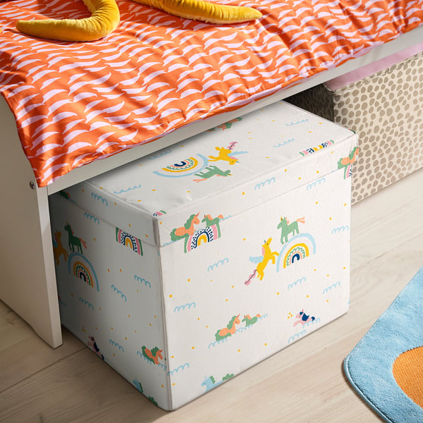 White STJÄRNSKOTT box with unicorns & rainbows fits under small bed with orange patterned mattress.