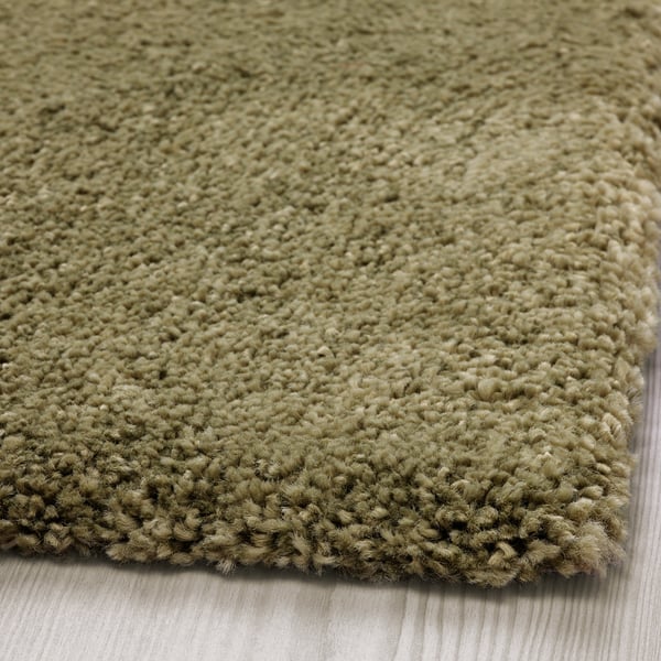 Rug close-up: soft, thick pile; light olive-green tone; disposed on wooden floor, reveals quality texture.