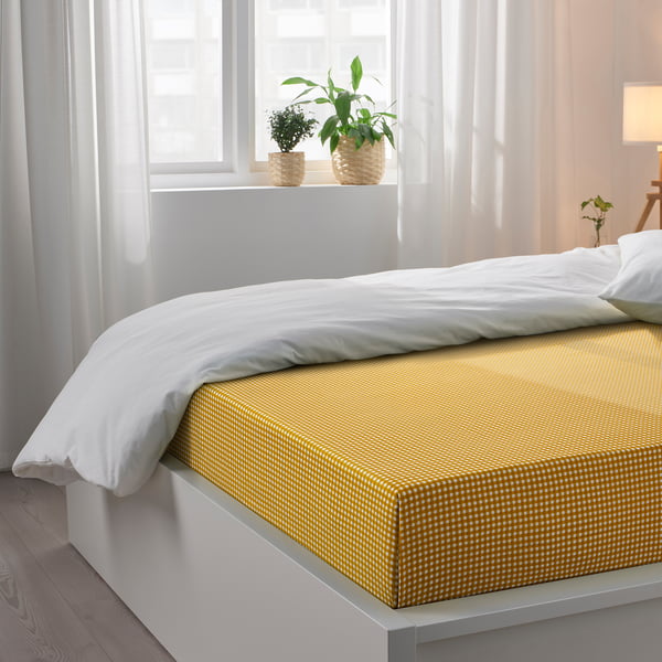 Yellow-checkered bed sheet set on white bed with pillows and plants.