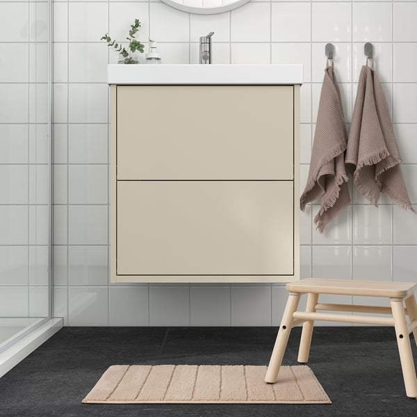 Beige recycled polyester bath mat in bathroom, soft, in front of cream vanity, near wooden bench.