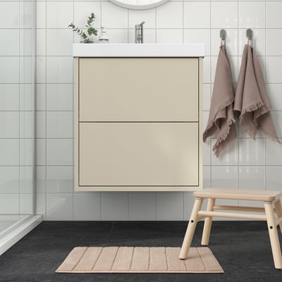 Beige recycled polyester bath mat in bathroom, soft, in front of cream vanity, near wooden bench.