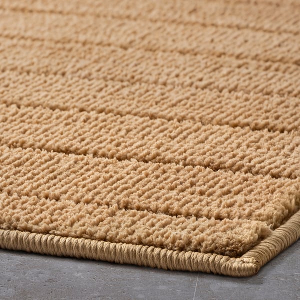 Close-up of a textured, beige bath mat with a braided edge, showcasing its soft, looped surface and durable construction.
