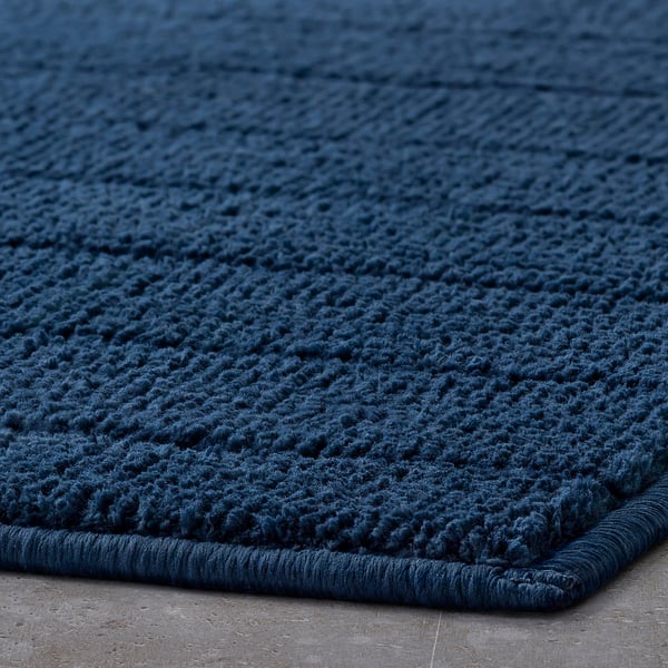 Dark blue, textured bath mat with a cosy, plush surface and weighted edge, ideal for comfort and quick drying.