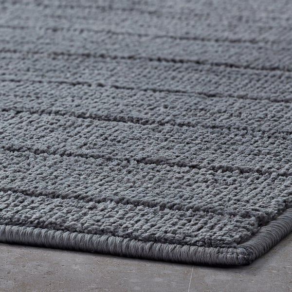 Close-up of a plush, grey bath mat with a soft, textured surface and a bordered edge, designed for comfort and quick drying.
