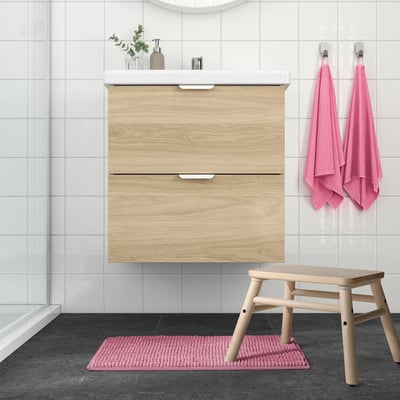 Bathroom with light wooden vanity, pink accessories, and TOFTBO mat on dark floor.