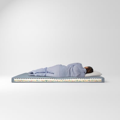 Person sleeping on blue firm mattress, white pillow, colourful border, minimalist room.