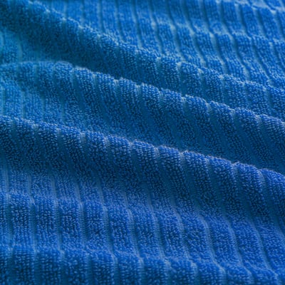 Bright blue VÅGSJÖN towel hangs neatly on a hook, displaying its soft cotton texture and ribbed design.