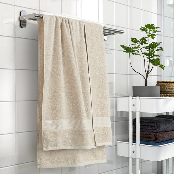 Beige VITBACKEN towel on rail, soft & absorbent, loop for hanging, near tiles, shelves with towels, plant.