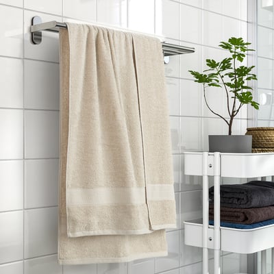 Beige VITBACKEN towel on rail, soft & absorbent, loop for hanging, near tiles, shelves with towels, plant.