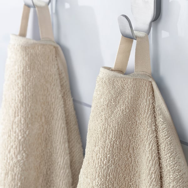Two beige bath towels hang on hooks, one with a loop for easy hanging.