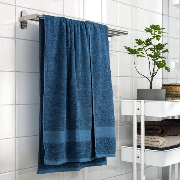 Blue VITBACKEN towel on a silver rail beside a white rack with folded towels and a potted plant.