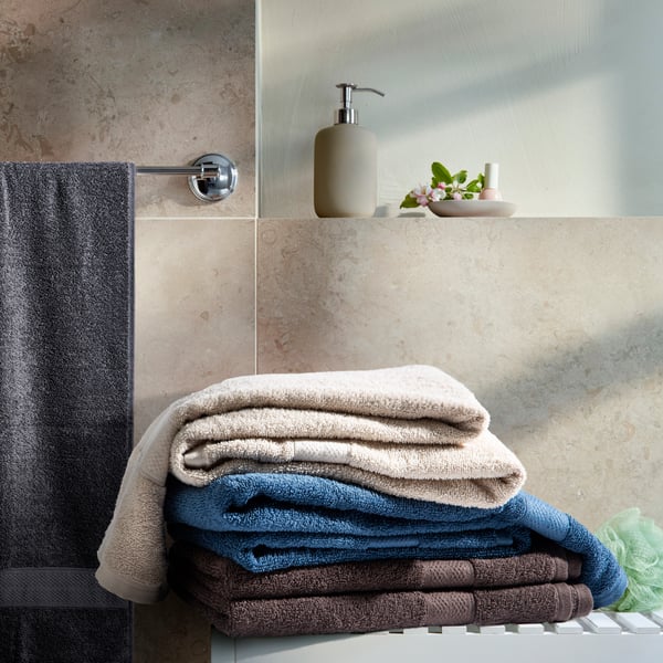 Bathroom with neatly stacked towels: white, blue, and brown on a beige tiled wall.