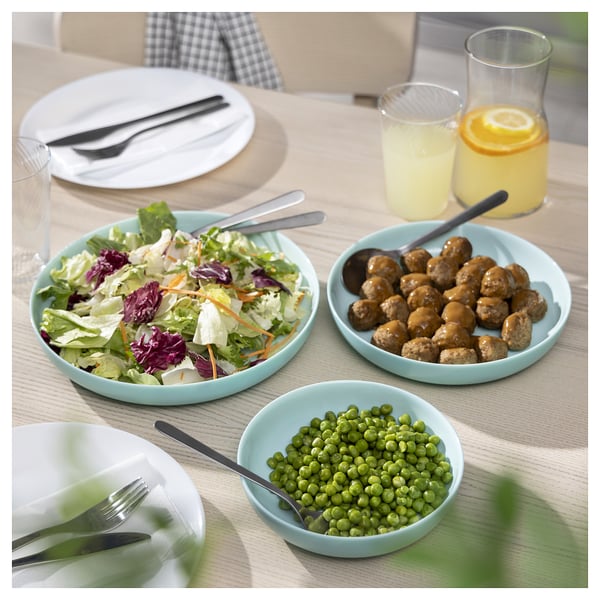 Bright turquoise dinnerware set with salad, peas, meatballs, and juices, made of durable tempered glass.