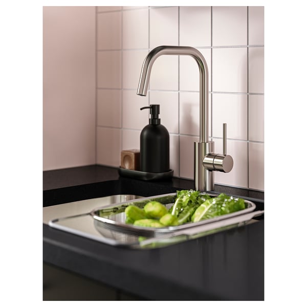 Rubinetto da cucina moderno in acciaio inox con arco alto sopra il lavello riempito con verdure verdi.