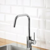 Rubinetto da cucina cromato moderno con beccuccio ad arco alto su bancone in legno.
