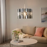 Soggiorno moderno con lampada a sospensione ÄLVSTARR, tavolino rotondo, cuscini rossi, verde, luce soffusa.