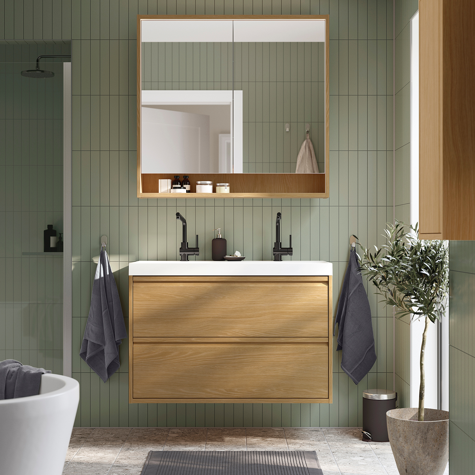 Bagno moderno con lavabo ÄNGSJÖN in rovere, grande lavabo, pareti verdi, specchio con mensole, asciugamani blu e ulivo.