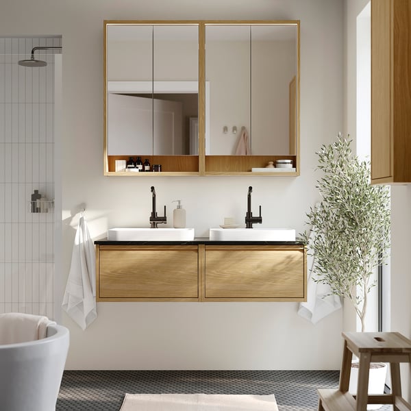 Elegante bagno con doppio lavabo in rovere ÄNGSJÖN, due lavandini bianchi, rubinetti neri, grande armadietto a specchio, asciugamani puliti e piante.