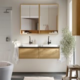 Elegante bagno con doppio lavabo in rovere ÄNGSJÖN, due lavandini bianchi, rubinetti neri, grande armadietto a specchio, asciugamani puliti e piante.
