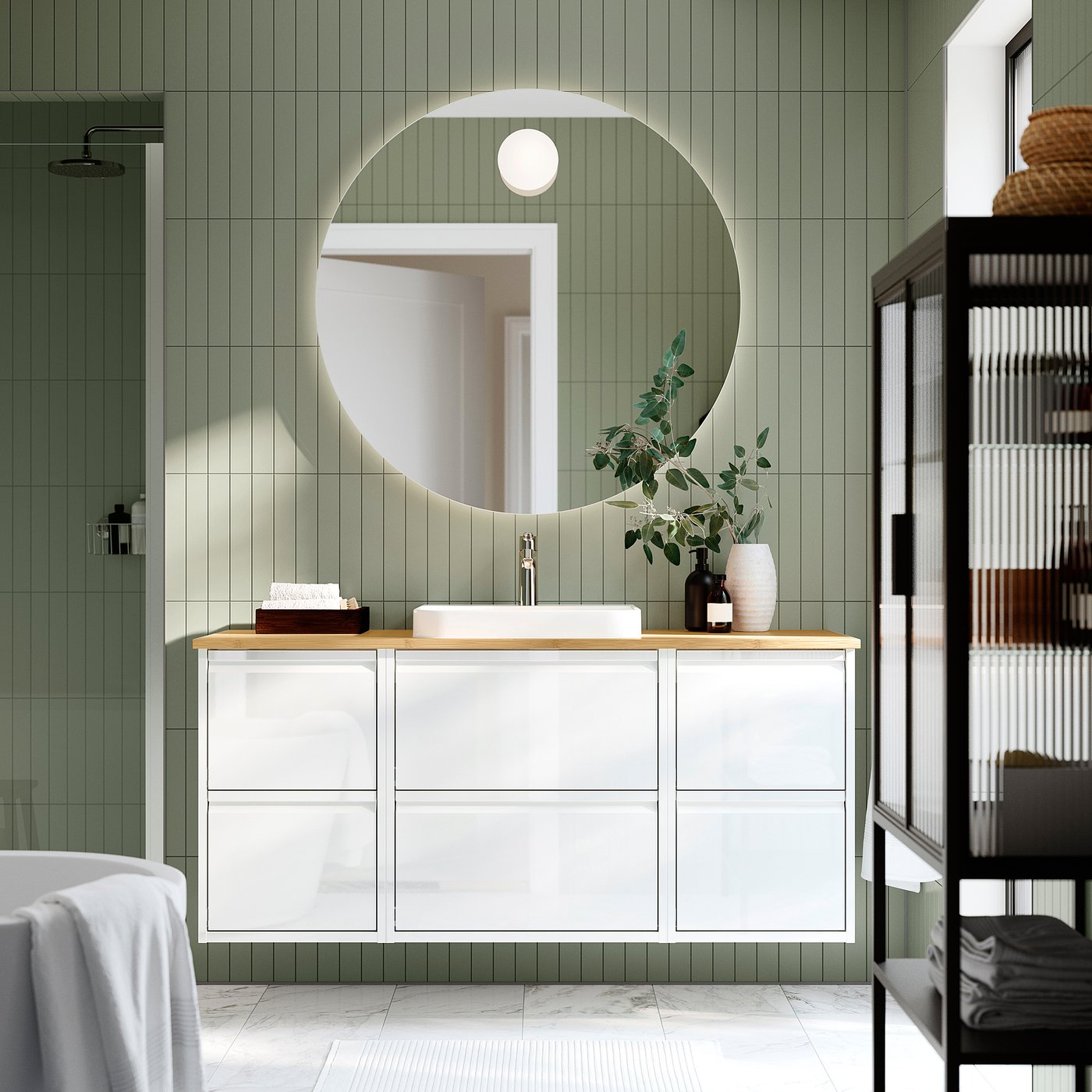 Bagno moderno con lavabo ÄNGSJÖN bianco, specchio rotondo, pareti verdi, pavimento in marmo e mensola nera. Lavello e piano di lavoro sono centrali e spaziosi.