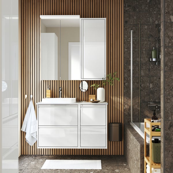 Moderno lavabo bianco con 4 ripiani, lavandino, specchio e accenti in legno. Montaggio a parete, ampio spazio di archiviazione, sensazione di apertura. Doghe di legno e pareti in marmo, piccolo tappeto.
