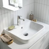 Moderna configurazione del lavandino del bagno con piano di lavoro bianco, rubinetto argentato, sapone e portasciugamani.