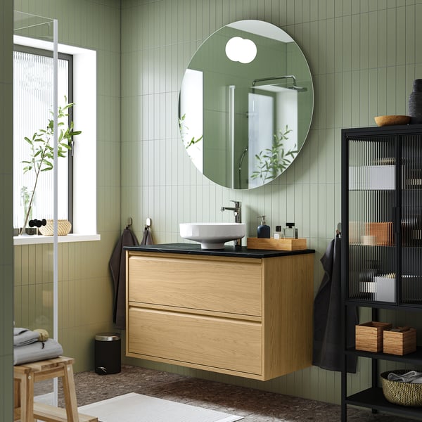 Bagno moderno con lavabo in legno, specchio, piastrelle verdi, bancone nero lucido.