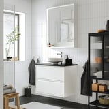 Moderno bagno bianco con lavabo ÄNGSJÖN, lavabo rotondo, grande specchio, accenti neri e piante.