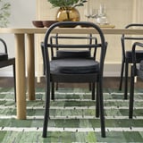Set da pranzo moderno con sedie in metallo nero e tavolo in legno. Le sedie hanno cuscini grigi e il tavolo contiene oggetti decorativi.