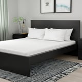 Camera da letto moderna con letto ÅKREHAMN nero, materasso a fantasia orchidea, tavolini, tappeto e tende.