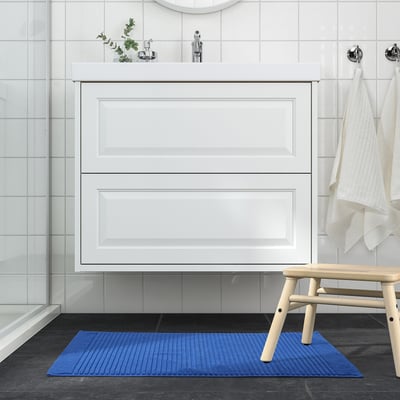 Bagno moderno con tappetino da bagno blu a contrasto con pavimento scuro.
