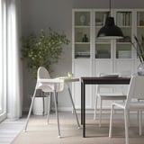 Piccola zona pranzo con seggiolone, tavolo, sedie, lampada a sospensione, tappeto, libreria e pianta ANTILOP.