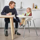 L'uomo si siede a tavola con il caffè, il bambino in seggiolone sorride accanto a lui.