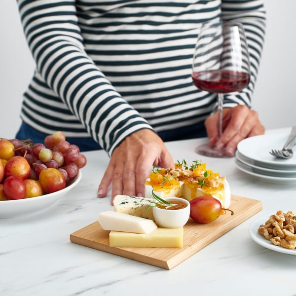 Mano che raggiunge il formaggio su una tavola di bambù con frutta, noci e vino.