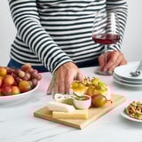 Mano che raggiunge il formaggio su una tavola di bambù con frutta, noci e vino.
