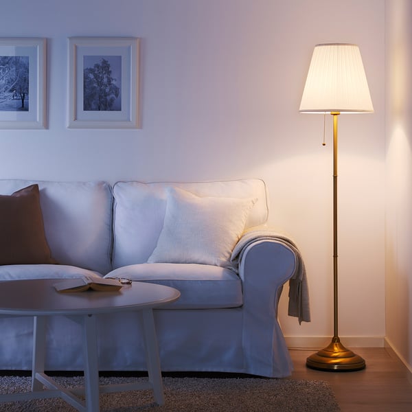 Accogliente soggiorno con lampada e divano ÅRSTID azzurri, tavolino in legno e arte da parete. Il paralume bianco delle lampade diffonde una luce soffusa.