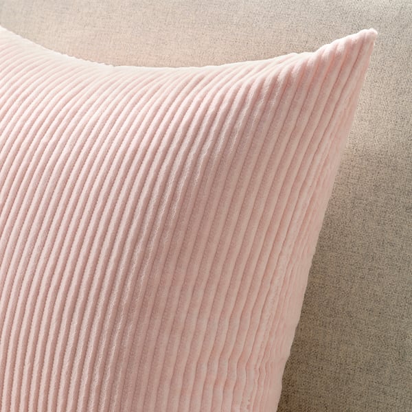 Primo piano di un morbido cuscino di velluto a coste rosa chiaro su un divano neutro. La trama è visibile, evidenziando la sua qualità accogliente e durevole.