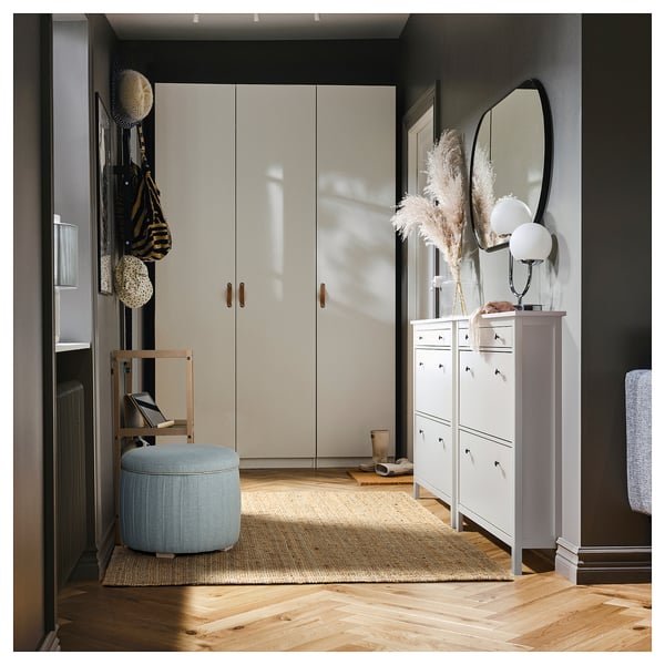 Ingresso moderno con armadio beige, pouf portaoggetti blu, scarpiera bianca, fiori secchi e specchio rotondo.