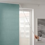 Persona che apre la tenda a rullo color verde acqua per far entrare la luce, montata accanto alla foto del paesaggio incorniciata.