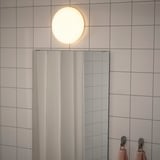 Una moderna plafoniera emette una luce morbida e uniforme in un bagno piastrellato, perfetta per illuminare lo spazio.