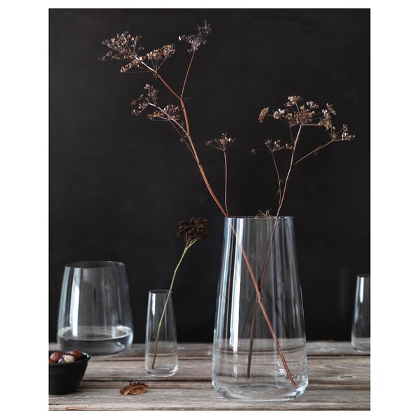 Vaso in vetro trasparente con fiori secchi su tavolo in legno. Arredamento minimalista con bicchierini e ciotola.