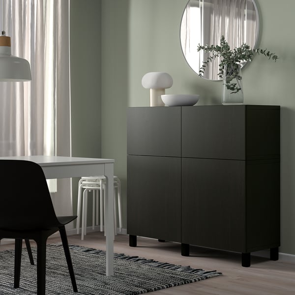 Spazio abitativo moderno con mobile BESTÅ nero, parete verde, scrivania bianca, specchio, lampade e piante.