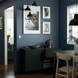 Moderna sala da pranzo con pareti blu scuro, credenza BESTÅ, scaffali, decorazioni e sedie bianche.