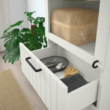 Armadio bianco aperto con portaposate e cassetto, pianta verde nelle vicinanze.