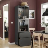 Cucina moderna con mobile alto BESTÅ grigio scuro, porte in vetro, sedie in legno e pareti marroni.