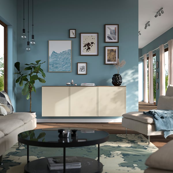 Salottino moderno con pareti color turchese, credenza bianca BESTÅ , tavolino da caffè in vetro, divano grigio e tappeto a motivi. Opere d'arte esposte sopra il credinetto.