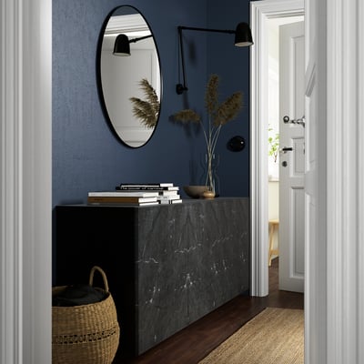 Moderno mobile contenitore BESTÅ da ingresso con elegante superficie in marmo, specchio circolare e lampade da parete. Il cestino sottostante offre ulteriore spazio di archiviazione.