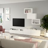 Soggiorno moderno: mobile tv BESTÅ, mensole a muro, divano grigio, cuscini rosa, tavolino, pianta.