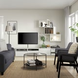 Soggiorno moderno con mobile tv BESTÅ, tv a schermo piatto, divano grigio, tavolino in vetro e mensole a muro.