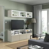 Soggiorno moderno con mobile tv BESTÅ, librerie, pensili, divano grigio e grande finestra con tende.